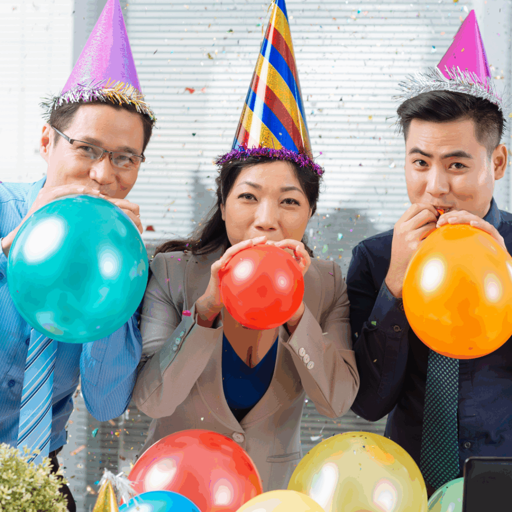 Employees wearing party hats and blowing up balloons