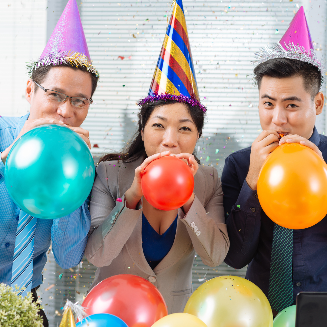 Employees wearing party hats and blowing up balloons