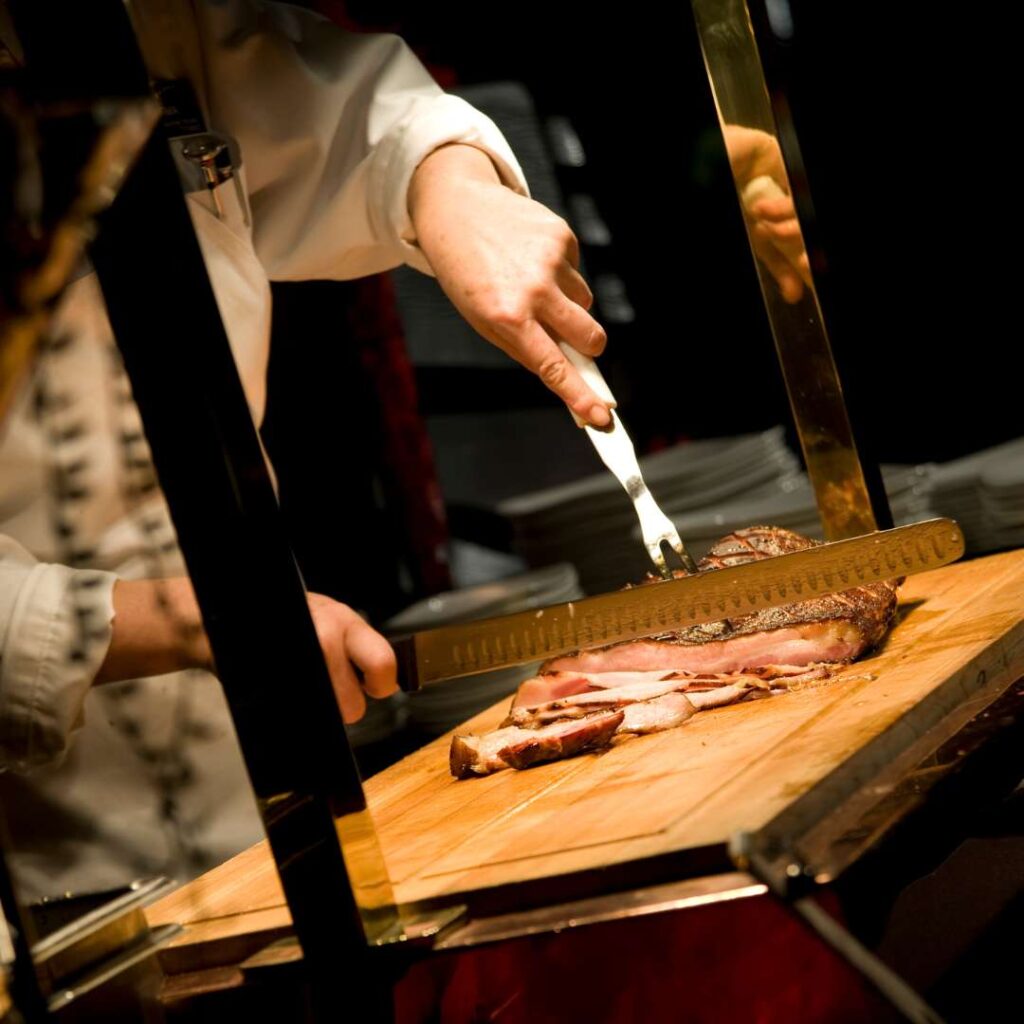Beautifully cooked beef being sliced by a chef with a large knife and fork under a bright light
