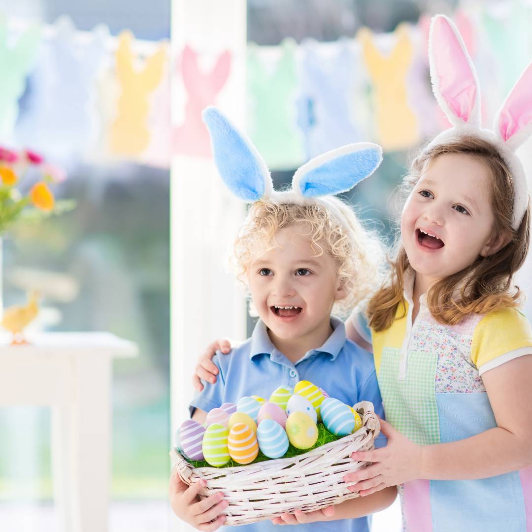A young girl and boy wearing bunny ears and holding a basket of colorful easter eggs with huge smiles on their faces.