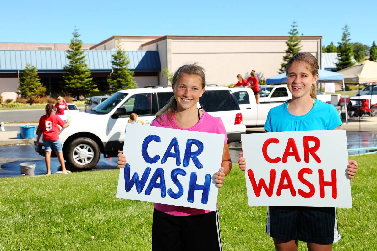 2 girls holding car wash signs for a school fundraiser